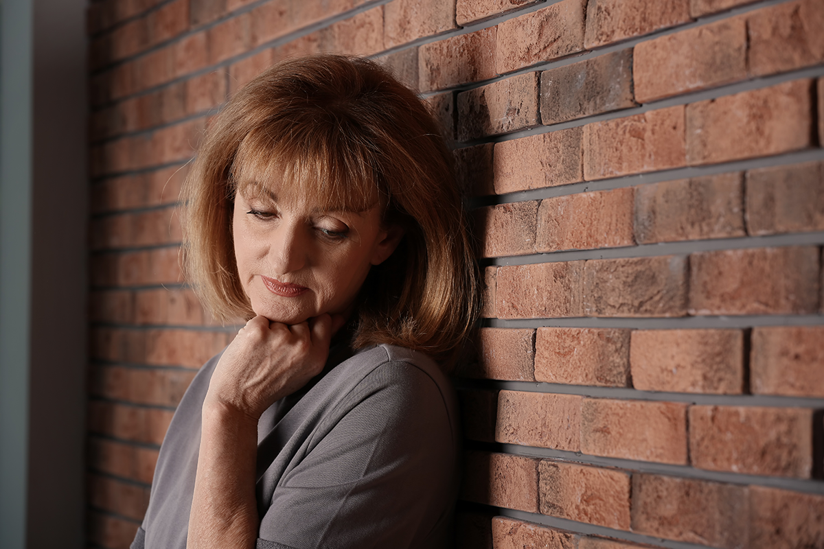 Senior woman suffering from depression near brick wall