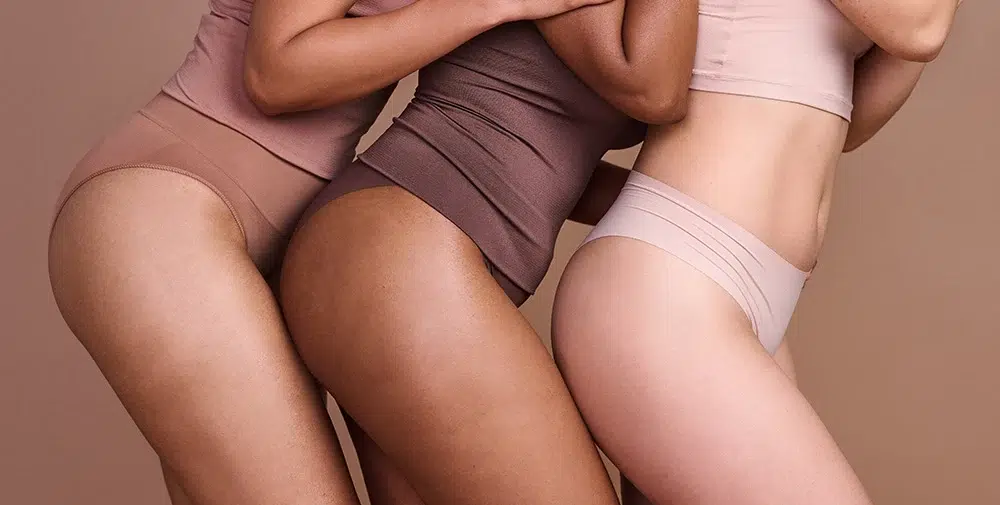 Three women in various shades of underwear standing close together.