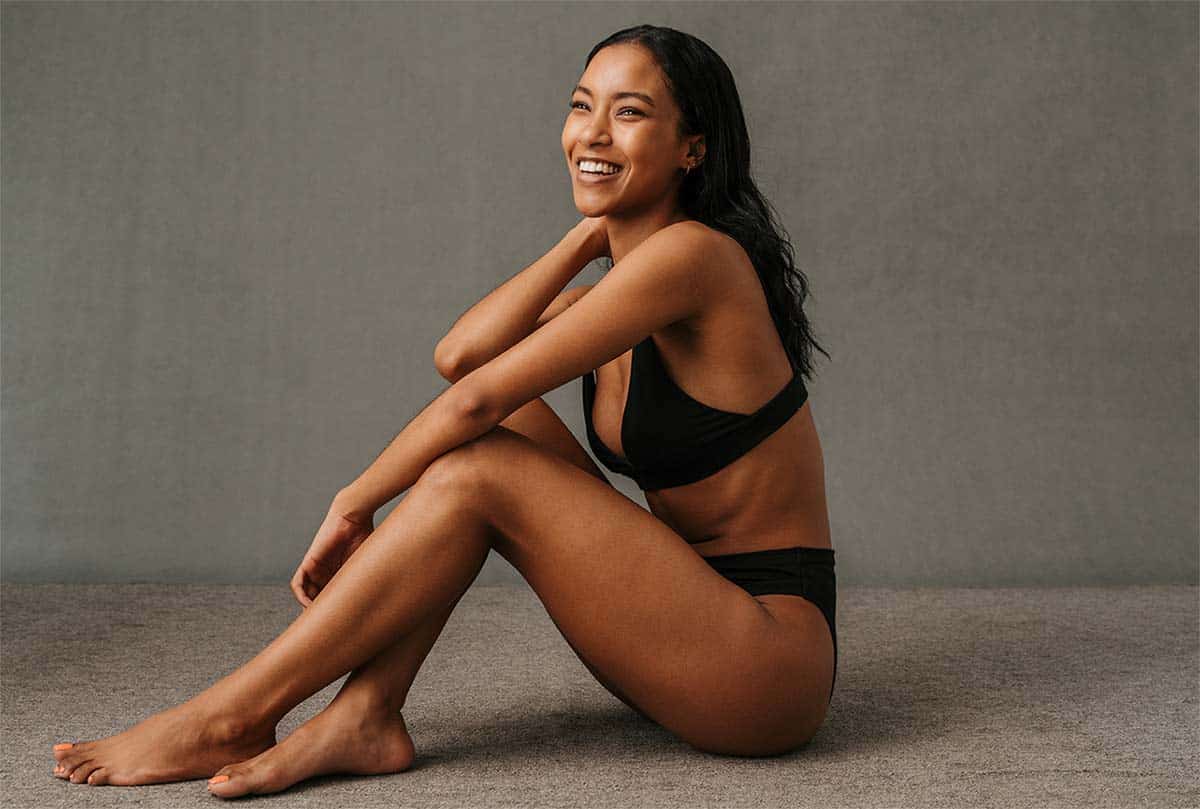young brown skinned woman sitting on the ground and posing in black underwear